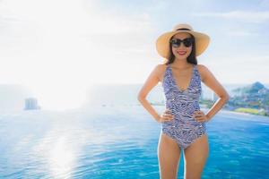 Retrato hermosa joven mujer asiática sonrisa feliz relajarse alrededor de la piscina en el hotel resort con vista al mar y al océano foto