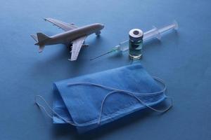 Glass bottle with medicine, syringe, disposable mask and figure of an airplane on the blue surface photo