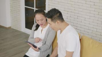 couple de famille asiatique mari et femme travaillent et utilisent une tablette numérique. un couple d'amoureux joyeux sourit en faisant du shopping en ligne et en regardant les médias sociaux ensemble depuis la maison dans le salon, au ralenti
