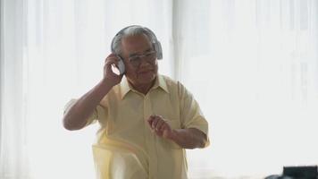 Asian elderly man or grandpa, happy senior retired guy with headphones listening music radio and moving dancing enjoying every moment of his funny life video