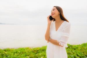 Portrait beautiful asian woman wear hat with smile happy for talking mobile phone on the beach photo