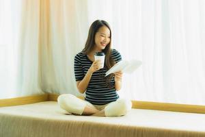 Portrait beautiful young asian woman reading book and hold coffee cup or mug in on sofa in living room area photo