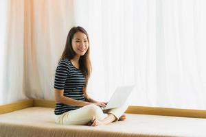 Portrait beautiful young asian woman using computer notebook or laptop on sofa in living room photo