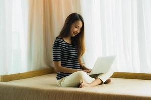 Retrato joven y bella mujer asiática con ordenador portátil o portátil en el sofá en la sala de estar foto