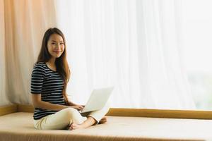 Portrait beautiful young asian woman using computer notebook or laptop on sofa in living room photo