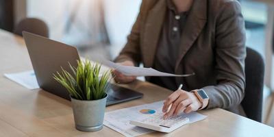 Mujer de negocios de cerca con calculadora y computadora portátil para hacer finanzas matemáticas en un escritorio de madera en la oficina y el fondo de trabajo empresarial, impuestos, contabilidad, estadísticas y concepto de investigación analítica foto