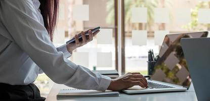 Primer plano de la imagen de una mujer sosteniendo y usando un teléfono móvil y use una computadora foto