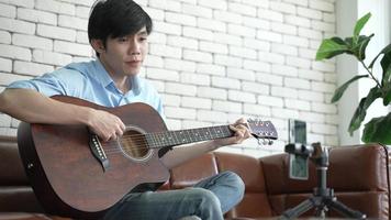 Young Asian Man Playing Guitar and Singing at Home to A Video Live Streaming