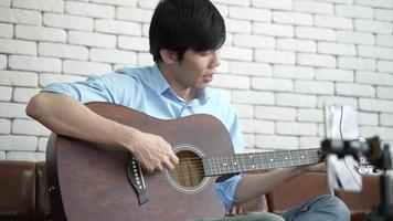 jovem asiático tocando violão e cantando em casa com uma transmissão ao vivo de vídeo
