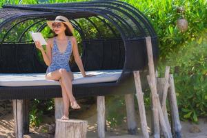 Portrait beautiful young asian woman reading book with happy smile relax in lounge bed chair on the beach sea ocean for leisure photo