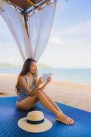 Portrait beautiful young asian woman reading book with happy smile relax in lounge bed chair on the beach sea ocean for leisure photo