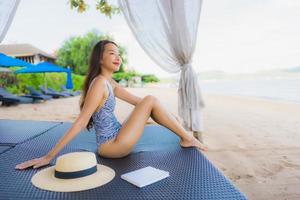 Portrait beautiful young asian woman reading book with happy smile relax in lounge bed chair on the beach sea ocean for leisure photo