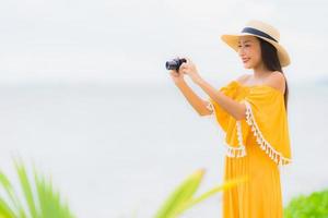 Retrato hermosa mujer asiática usar sombrero con sonrisa feliz ocio en tomar una foto en la playa y el mar en vacaciones de vacaciones