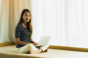 Portrait beautiful young asian woman using computer notebook or laptop on sofa in living room photo