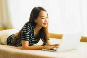 Portrait beautiful young asian woman using computer notebook or laptop on sofa in living room photo