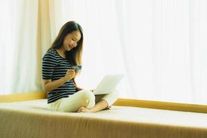 Retrato joven y bella mujer asiática con ordenador portátil o portátil con tarjeta de crédito para ir de compras foto