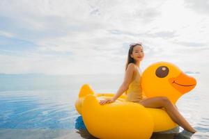 Retrato joven mujer asiática en flotador inflable pato amarillo alrededor de la piscina al aire libre en el hotel y resort foto