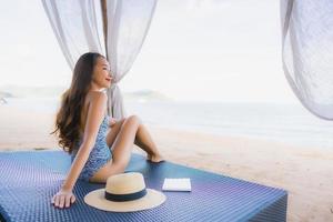 Portrait beautiful young asian woman reading book with happy smile relax in lounge bed chair on the beach sea ocean for leisure photo