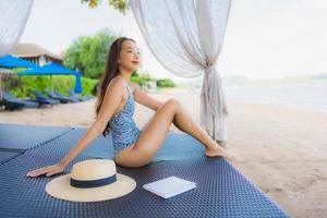 Portrait beautiful young asian woman reading book with happy smile relax in lounge bed chair on the beach sea ocean for leisure photo