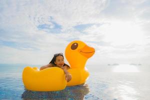 Portrait young asian woman on inflatable float yellow duck around outdoor swimming pool in hotel and resort photo