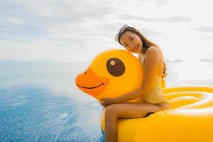 Retrato joven mujer asiática en flotador inflable pato amarillo alrededor de la piscina al aire libre en el hotel y resort foto