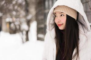 Hermosa joven asiática sonriendo feliz para viajar en la temporada de invierno con nieve