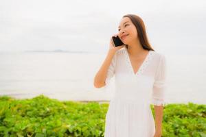 Portrait beautiful asian woman wear hat with smile happy for talking mobile phone on the beach photo