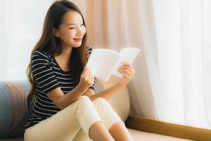 retrato, hermoso, joven, mujer asiática, libro de lectura, en, sofá, en, sala, área foto