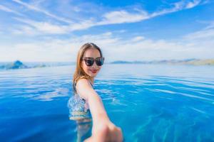 Portrait beautiful young asian woman smile happy relax around swimming pool in hotel resort with sea and ocean view photo