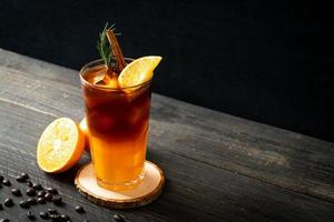 A glass of iced Americano black coffee and a layer of orange and lemon juice decorated with rosemary and cinnamon on a wood background photo