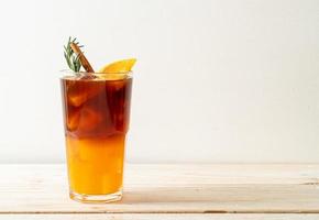 A glass of iced Americano black coffee and a layer of orange and lemon juice decorated with rosemary and cinnamon on a wood background photo