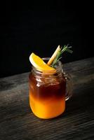 A glass of iced Americano black coffee and a layer of orange and lemon juice decorated with rosemary and cinnamon on a wood background photo