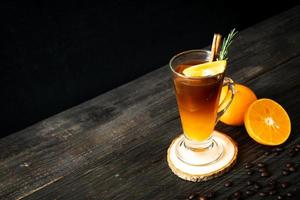un vaso de café negro americano helado y una capa de jugo de naranja y limón decorado con romero y canela sobre un fondo de madera