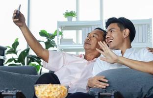 Asian father and son are happily taking selfies at home with their smartphones photo