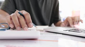 Close up of businessman or accountant hand holding pen working on calculator to calculate business data, accountancy document and laptop computer at office, business concept photo