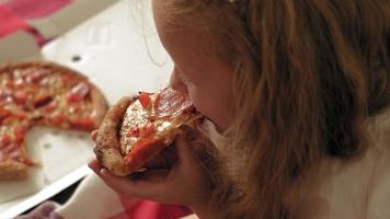 Preschooler girl eating pizza while sitting on floor in room video