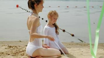 mãe e filha em maiôs brancos, dançando com uma fita de ginástica em uma praia arenosa. amanhecer de verão