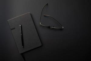 A picture of diary book of a student with eyeglasses and pencil on top on the black background photo