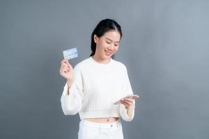 Young Asian girl showing plastic credit card while holding mobile phone photo