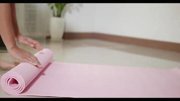 vrouw die roze yogamat rolt voor of na sportvoorbereiding die thuis in de woonkamer traint, fit sport vrouwelijke training door yoga te oefenen tijdens covid19 pandemie, sport gezond levensstijlconcept video