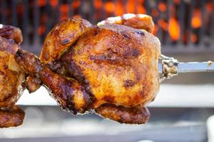 Roasted chickens on spit grilled over fire of a big barbecue photo