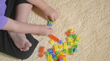 felice ragazzo asiatico in età prescolare che gioca con blocchi giocattolo di plastica creativi che restano a casa. divertente bambino seduto che costruisce una torre di blocchi colorati, concetto di gioco di costruzioni educative video