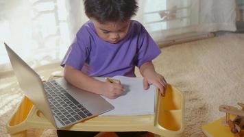 un enfant asiatique utilisant un ordinateur portable étudie une leçon en ligne à la maison. enseignement à distance à domicile, distance sociale pendant la quarantaine de covid-19, pas à l'école, concept d'enseignement à distance à domicile au ralenti
