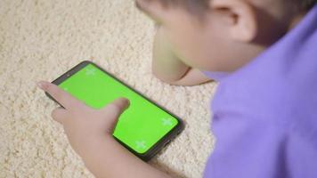 Asian kid boy preschool with gadget playing video games digital on mobile phone at home. Little child using and holding a smartphone green screen in hand, Technology generation concept