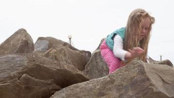 Girl plays over large stones on the seashore