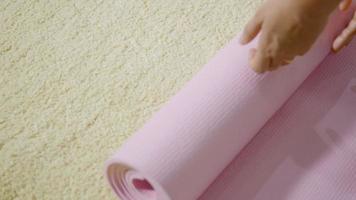 asiatisk ung kvinna rullande konditionyoga rosa matta innan sportövning för träning, kvinna som tränar hemma i vardagsrummet. livsstil sport hälsosamt koncept, slow motion från 60 fps