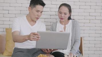lycklig asiatisk familj par man och hustru arbetar och använder bärbar dator analysera deras ekonomi diskutera. glada älskande par leende shopping beställa produkter online hemifrån via dator