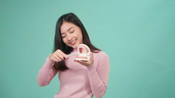 Aziatische jonge mooie vrouwenglimlach die model toont hoe de tanden met tandenborstel goed en juist schoon te maken, vrouwelijk borstel wit tandenmodel geïsoleerd op blauwe achtergrond, tandhygiëne en gezondheidsconcept video