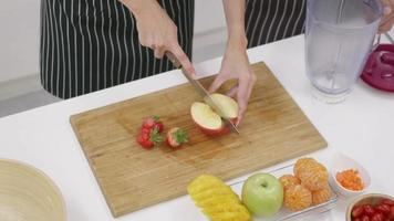 heureux asiatique belle jeune famille couple mari et femme faisant un smoothie frais dans la cuisine ensemble à la maison. l'homme et la femme tranchent des pommes et des légumes frais. concept de mode de vie sain video