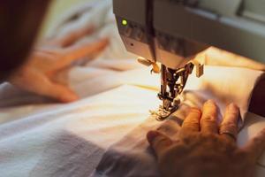 Close up hands of senior woman using sewing machine to sew clothes at home photo